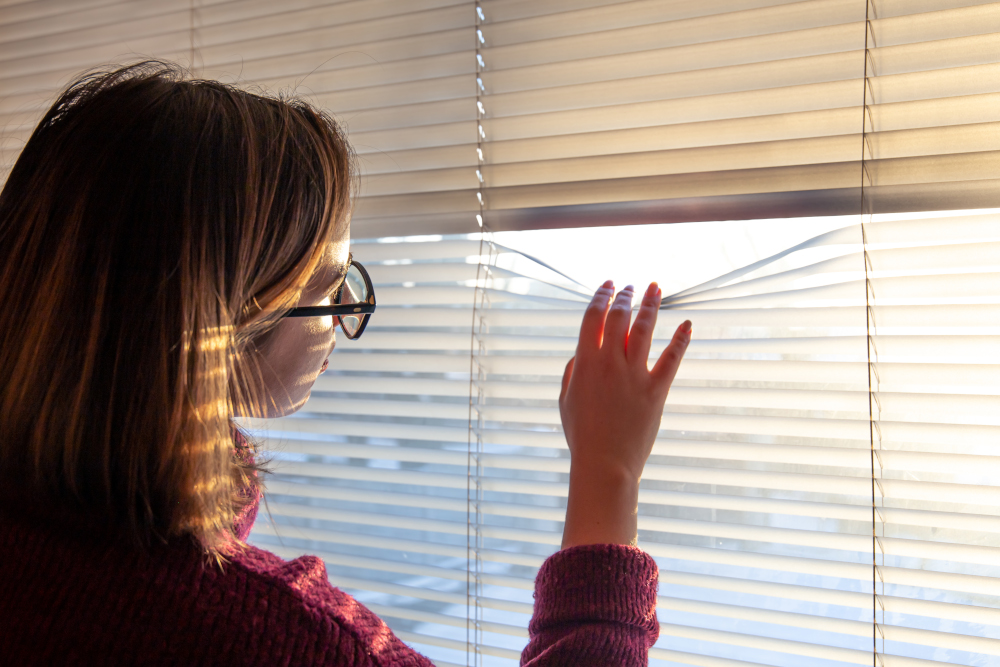 Personne regardant discrètement par une fenêtre, symbole de surveillance ou d'observation secrète.